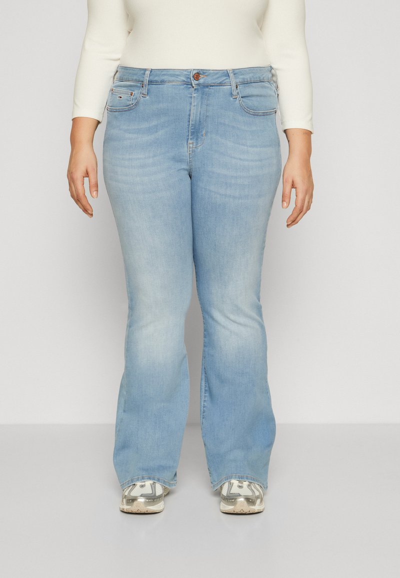 Helle blaue Bootcut-Jeans mit mittelhoher Taille, ausgestattet mit Fronttaschen und einer leichten Ausbleichung. Getragen mit gemusterten Sneakers.
