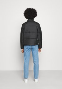 Czarna pikowana kurtka z wysokim kołnierzem i długimi rękawami, noszona na jasnoniebieskich dżinsach i białych trampkach.