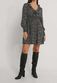 Vestido floral negro con mangas largas, cuerpo fruncido y escote en V. Combinado con botas de cuero negro de tacón cuadrado hasta la rodilla.