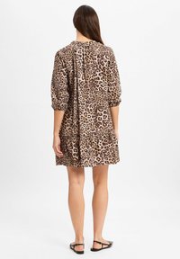 Leopardenmuster Kurzes Kleid mit langen Ärmeln, einem runden Ausschnitt und gerafftem Rückendetail. Weicher Stoff mit strukturiertem Muster. Schwarze flache Sandalen.