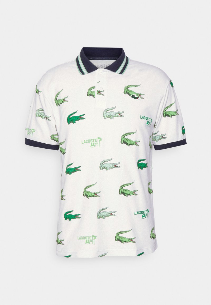 Polo blanc présentant des motifs répétés de crocodiles verts, avec un col marine et des accents rayés. Le tissu semble doux et respirant.