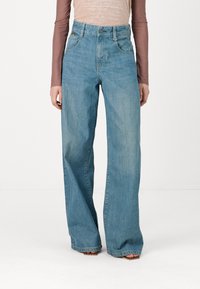 Blugi deschis la culoare, cu talie înaltă și croială largă, având un stil clasic cu cinci buzunare și ușoare decolorări pentru textură.