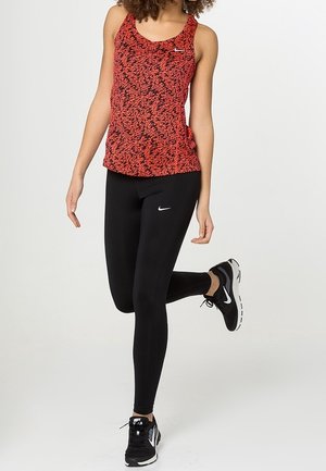 Rood en zwart patroon tanktop met een ronde hals, gecombineerd met zwarte leggings en zwarte sportschoenen. Opvallende Nike-logo's op de kleding.