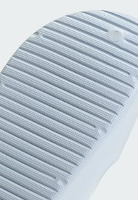 Suola di scarpa in gomma bianca con scanalature testurizzate e piccole rientranze circolari, caratterizzata da una finitura liscia e una forma uniforme.