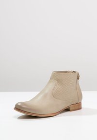 Beiger Leder-Stiefelette mit perforiertem Design, abgerundeter Spitze und niedrigem Holzabsatz. Mit seitlichem Reißverschluss für einfaches An- und Ausziehen.