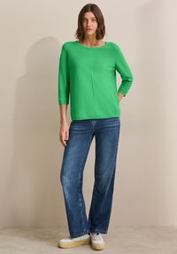 Haut en maille léger vert avec un décolleté arrondi et des manches trois-quarts, associé à un jean en denim bleu à jambes larges et des baskets blanches.