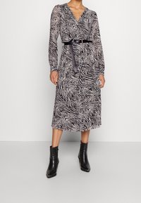 Vestido de manga larga con estampado de cebra en blanco y negro, diseño cruzado, cintura ceñida con cinturón y longitud midi, combinado con botas negras hasta el tobillo.