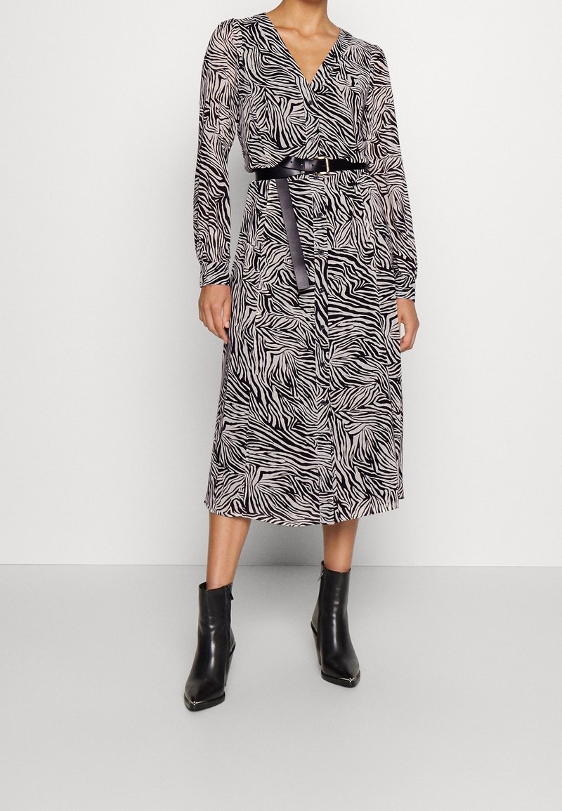 Vestido de manga larga con estampado de cebra en blanco y negro, diseño cruzado, cintura ceñida con cinturón y longitud midi, combinado con botas negras hasta el tobillo.