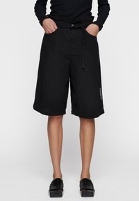 Zwarte shorts met een trekkoord in de taille, twee zijzakken, een losse fit en een logo detail op het onderbeen. Gemaakt van een gestructureerde stof.
