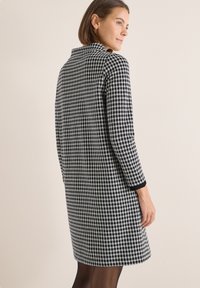Czarna i biała sukienka w kratę z długimi rękawami, okrągłym kołnierzykiem i teksturowanym materiałem. Zawiera czarne akcenty przy mankietach.