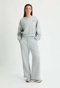 Sudadera gris y pantalones de chándal de pierna ancha hechos de una tela suave, con cuello redondo, cinturilla elástica y un pequeño logo en el pecho.