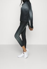 Abbigliamento sportivo con un top a maniche lunghe in gradiente nero e leggings con pannelli laterali. Scarpe da ginnastica bianche completano l'outfit.