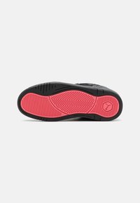 Semelle de basket noire et rose avec motifs de grip texturés et un logo circulaire près du talon sur fond blanc uni.