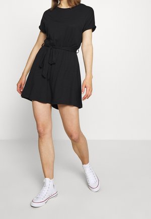 Schwarzes Freizeitkleid mit kurzen Ärmeln, einem runden Ausschnitt und einem Stoffgürtel in der Taille. Kombiniert mit weißen High-Top-Sneakern.