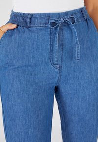 Pantalones jogger de denim azul con cinturilla elástica y cordón de ajuste. Cuenta con bolsillos laterales y una tela suave y texturizada.