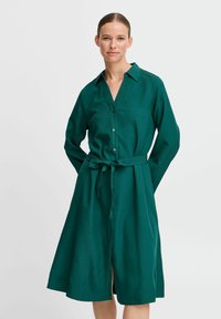 Grünes Hemdkleid mit langen Ärmeln, durchgehender Knopfleiste und gebundenem Taillengürtel. Aus einem glatten Stoff gefertigt, mit Kragen und Rock in mittellanger Länge.