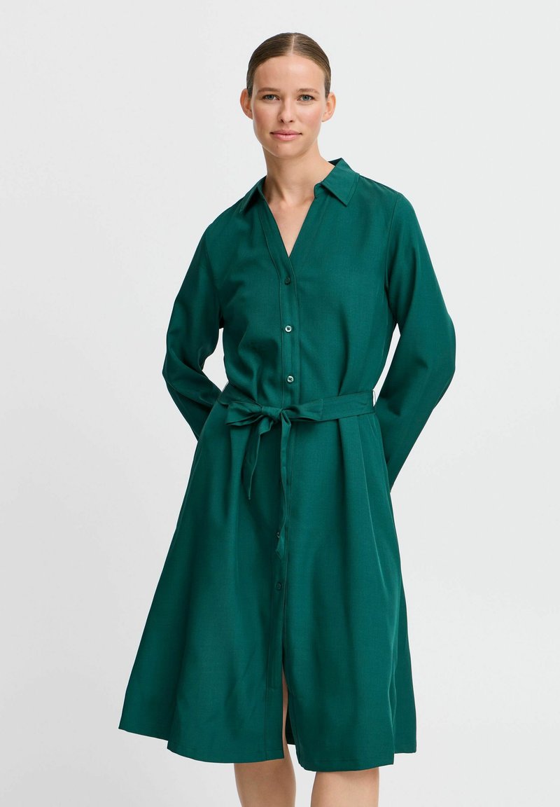 Grünes Hemdkleid mit langen Ärmeln, durchgehender Knopfleiste und gebundenem Taillengürtel. Aus einem glatten Stoff gefertigt, mit Kragen und Rock in mittellanger Länge.