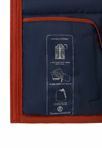 Marineblauer und orangefarbener Weste mit gedruckten Anweisungen zum Verpacken in eine Tasche: falten, rollen, schließen und bereit zum Mitnehmen, markiert mit Thomas Goodwin.