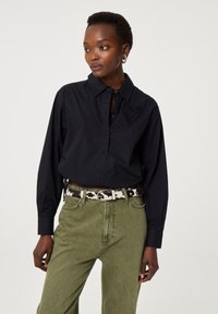 Zwarte overhemd met een textured hartdetail op de borst, gecombineerd met olijfgroene broek en een gestreepte riem.