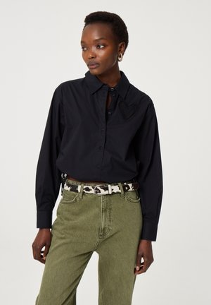 Zwarte overhemd met een textured hartdetail op de borst, gecombineerd met olijfgroene broek en een gestreepte riem.