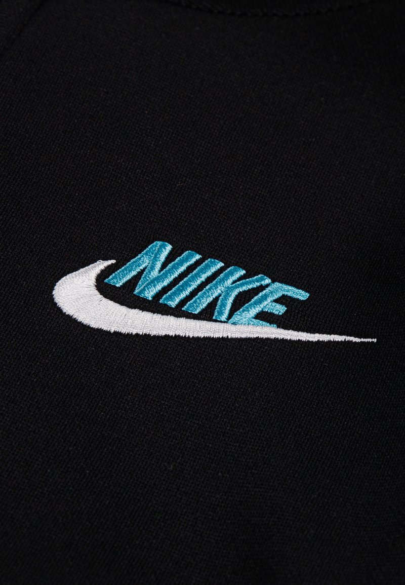 Tela negra con un destacado logo de Nike bordado en aqua y blanco, con un diseño de swoosh y detalles de costura texturizada.