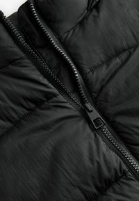 Svart puffjacka med detaljer som en blank dragkedja, quiltad textur och slät yta, vilket framhäver materialets lätta utseende.