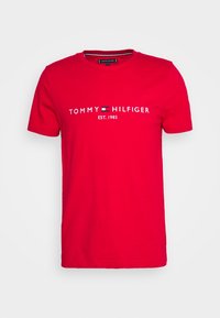 Punainen puuvillainen t-paita lyhyillä hihoilla, pyöreällä kaula-aukolla, jossa lukee "TOMMY HILFIGER" ja pieni logomalli valkoisena ja sinisenä.