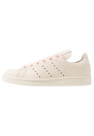 Baskets basses beiges Adidas avec motifs triangulaires perforés sur le côté, semelle beige assortie et œillets roses clairs.