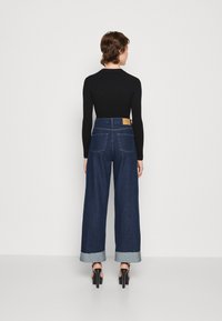 Pantalones vaqueros de pierna ancha en azul oscuro con un dobladillo descolorido, que cuentan con una etiqueta marrón en la cinturilla, combinados con una blusa negra ajustada de manga larga.