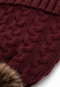 Berretto a maglia color bordeaux con motivo a trecce e risvolto, impreziosito da un pompon in ecopelliccia. Tessuto morbido e filato spesso.