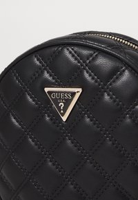 Borsa in ecopelle trapuntata nera con una targa logo triangolare dorata con la scritta "GUESS U.S.A." Apertura con zip sulla parte superiore.