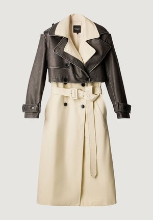 Gabardina bicolor con parte inferior crema con cinturón y parte superior y mangas cortas de cuero marrón oscuro, de doble botonadura y cuello ancho.