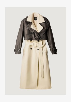 Gabardina bicolor con parte inferior crema con cinturón y parte superior y mangas cortas de cuero marrón oscuro, de doble botonadura y cuello ancho.