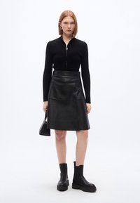 Μαύρος ριμπ πλεκτός πουλόβερ με φερμουάρ στο ντεκολτέ, συνδυασμένος με μαύρη δερμάτινη φούστα Α-γραμμή. Ολοκληρωμένο με chunky μαύρα μποτάκια αστραγάλου και μία μικρή τσάντα.