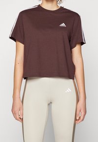 Brun, kortärmad t-shirt med vit Adidas-logotyp på bröstet; matchad med krämfärgade tajta leggings.