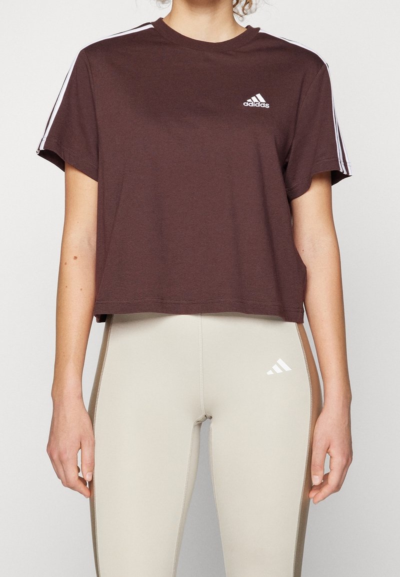 Brun, kortärmad t-shirt med vit Adidas-logotyp på bröstet; matchad med krämfärgade tajta leggings.