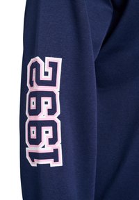 Marineblauses Hemd mit langen Ärmeln und einem weißen und pinken Grafikdruck mit der Aufschrift "1992" auf dem Ärmel. Hergestellt aus Baumwolle mit glatter Textur.