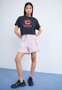Tricou scurt negru cu grafică florală colorată; pantaloni scurți roz deschis cu talie elastică și buzunare laterale; adidași sport negri.
