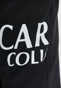 Schwarzer Sweatshirt mit auffälligem weißen Text, der "CAR" und "COLL." zeigt. Der Stoff ist weich, strukturiert und leicht abgenutzt in der Nähe der Schrift.