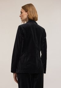 Czarna aksamitna marynarka o eleganckim fasonie, dopasowany krój, klapy z wcięciem oraz gładka faktura, z pojedynczym rozcięciem z tyłu i długimi rękawami.