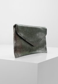 Pochette métallique verte avec un motif texturé en peau de serpent, dotée d'un accent en métal argenté en forme de triangle et d'un design épuré et minimaliste.
