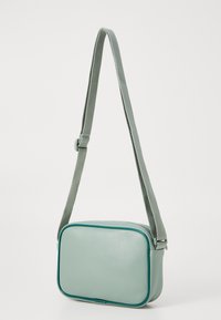 Borsa a tracolla verde menta con forma rettangolare, materiale in pelle testurizzata e rifiniture in verde scuro a contrasto. Include una tracolla regolabile.