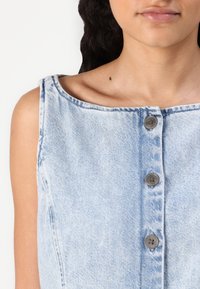 Helles blaues Denim-Ärmelloses Kleid mit weitem Ausschnitt, fünf funktionalen grauen Knöpfen entlang der Vorderseite und einer leicht verblassten Textur.