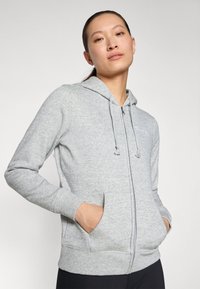 Hallide halliga tõmblukkidega kapuutsiga sjahe hall fashion kapuuts, pehme materjal, tõmblukuga kapuuts, tõmblukud ja ees olevad taskud. Minimalistlik disain õrnalt logoga.