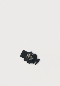 Μαύρο πλαστικό ηλεκτρονικό εξάρτημα με κυκλική τμήμα μπαταρίας και μια μικρή προεξέχουσα γλωττίδα, με χαραγμένο κείμενο στην ετικέτα της μπαταρίας.