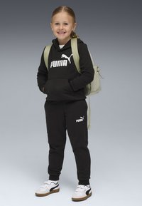 Haut à capuche noir et sweat-pants avec logo Puma blanc, associés à des chaussures blanches et marron. Sac à dos vert clair. Enfant souriant avec de longs cheveux.