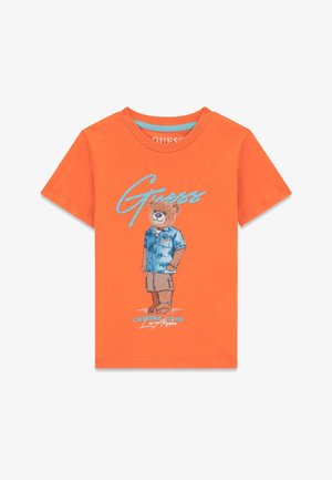 T-shirt orange à manches courtes avec un ours en peluche portant une chemise bleue et un short beige, logo "Guess" en bleu et texte "California Los Angeles" en dessous.