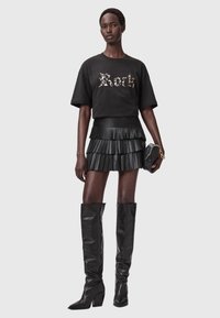 Musta T-paita graafisella tekstillä, kerrostettu musta volangihame, ja polvipituiset mustat nahkabootsit paksuilla koroilla. Mukana musta clutch-laukku.