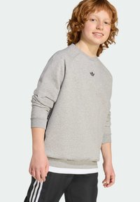 Šedá mikina s rebrovaným lemom a manžetami; má malú čiernu logo na hrudi. Nosená s čiernymi nohavicami s bielymi pruhmi.