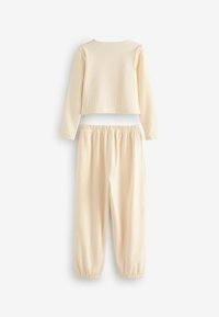 Cream-colored ribbed two-piece set featuring a cropped long-sleeve top and elastic-waist pants with elastic cuffs. Soft texture throughout.